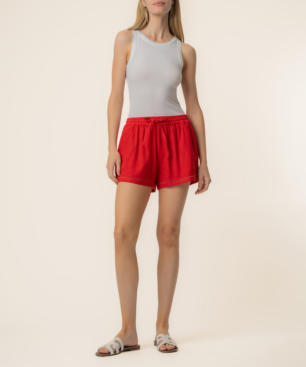 Woman wearing red linen shorts with drawstring waist and white sleeveless tank top.