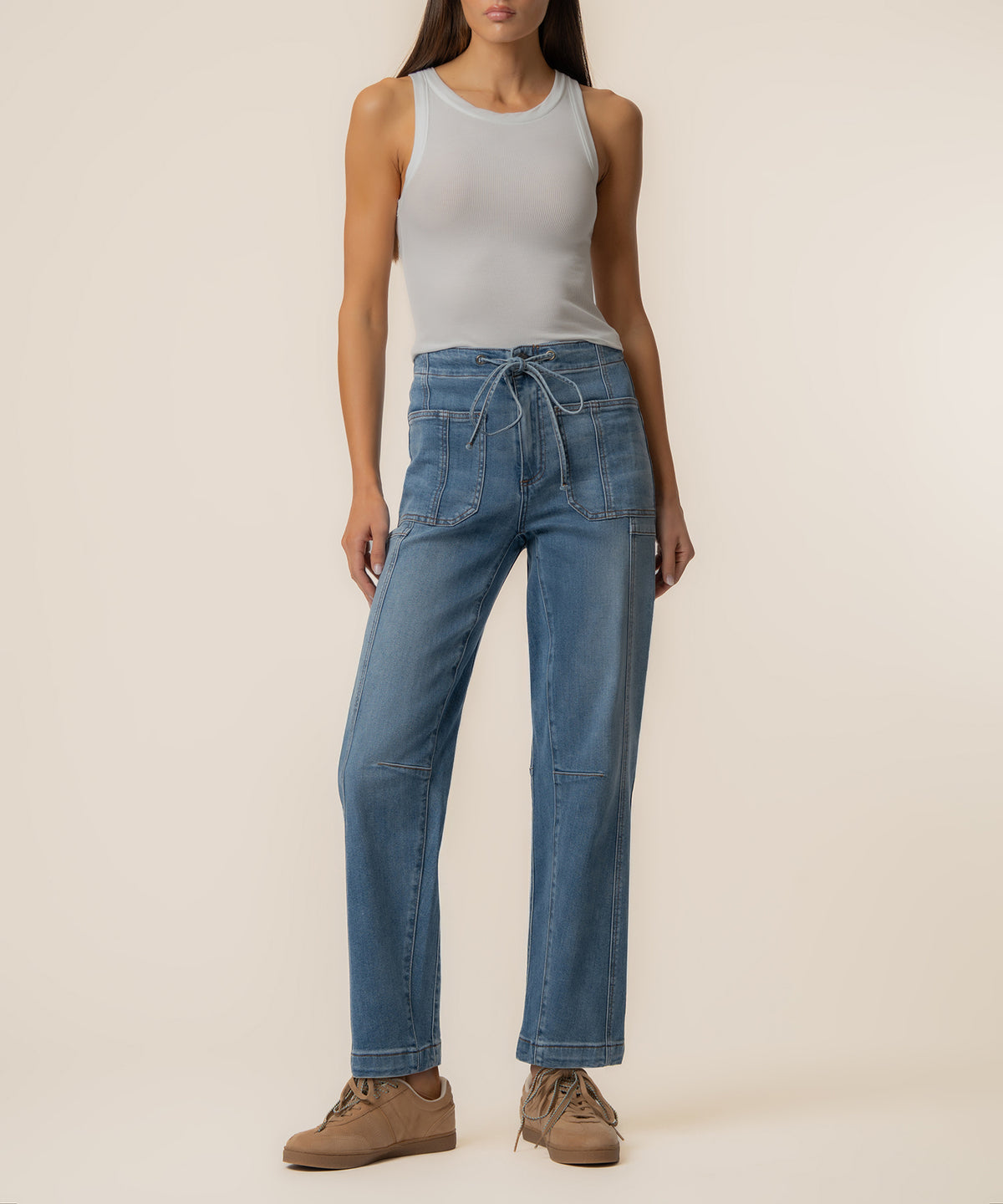 Woman wearing light gray sleeveless tank top and high-rise blue denim barrel jeans with drawstring waist.