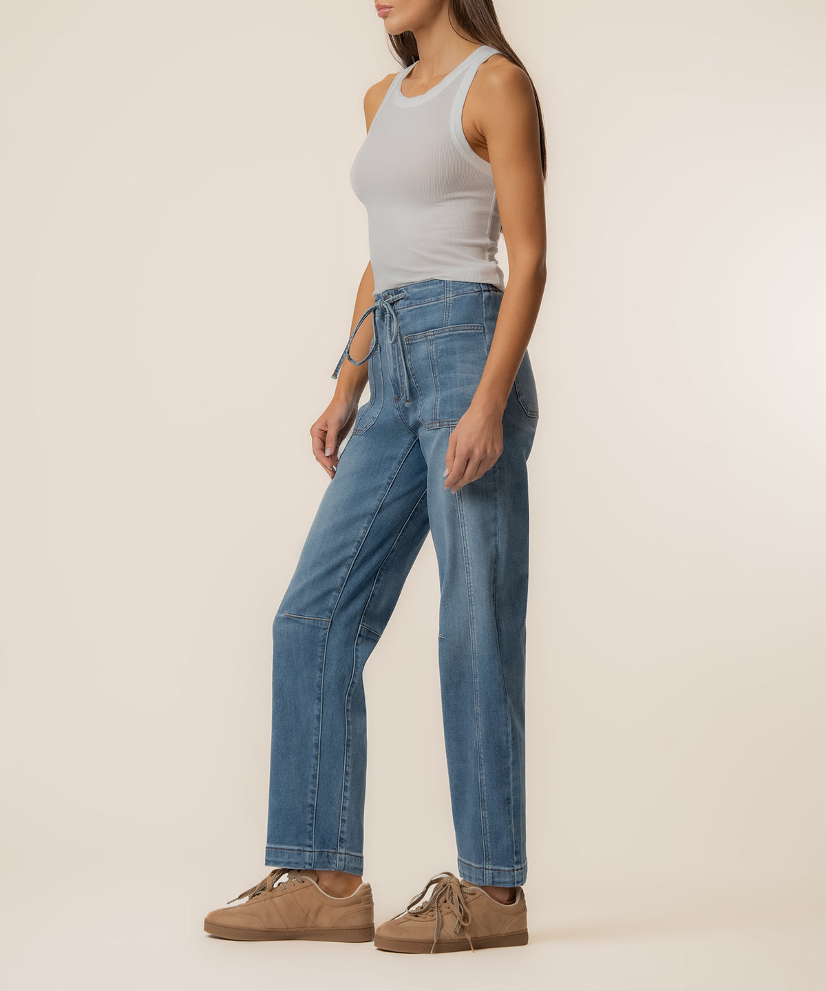 Woman wearing light gray sleeveless tank top and high-rise medium-wash slouchy barrel jeans with drawstring waist.