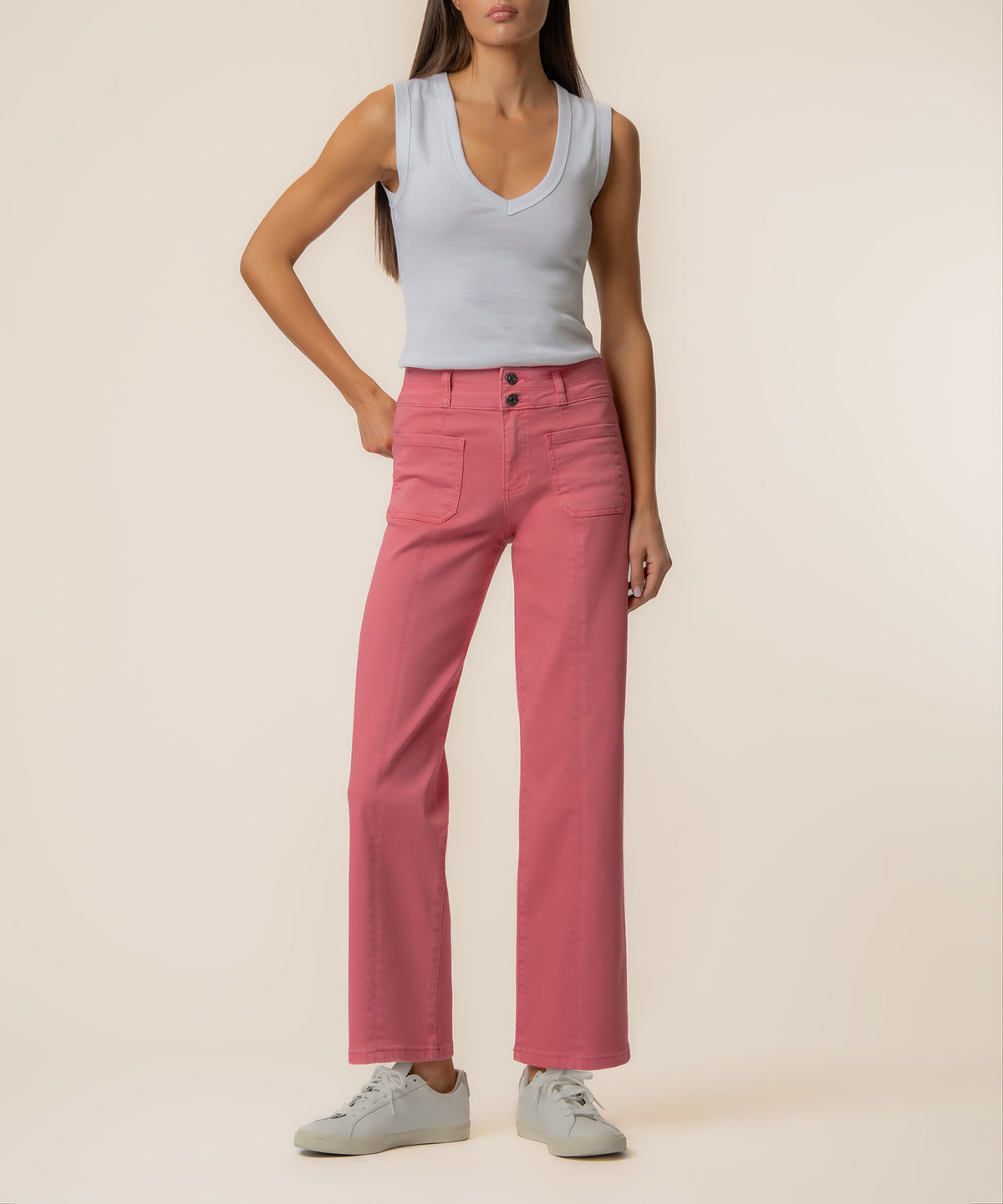 Woman wearing flamingo pink high-rise straight leg jeans with white sleeveless tank top and white sneakers.