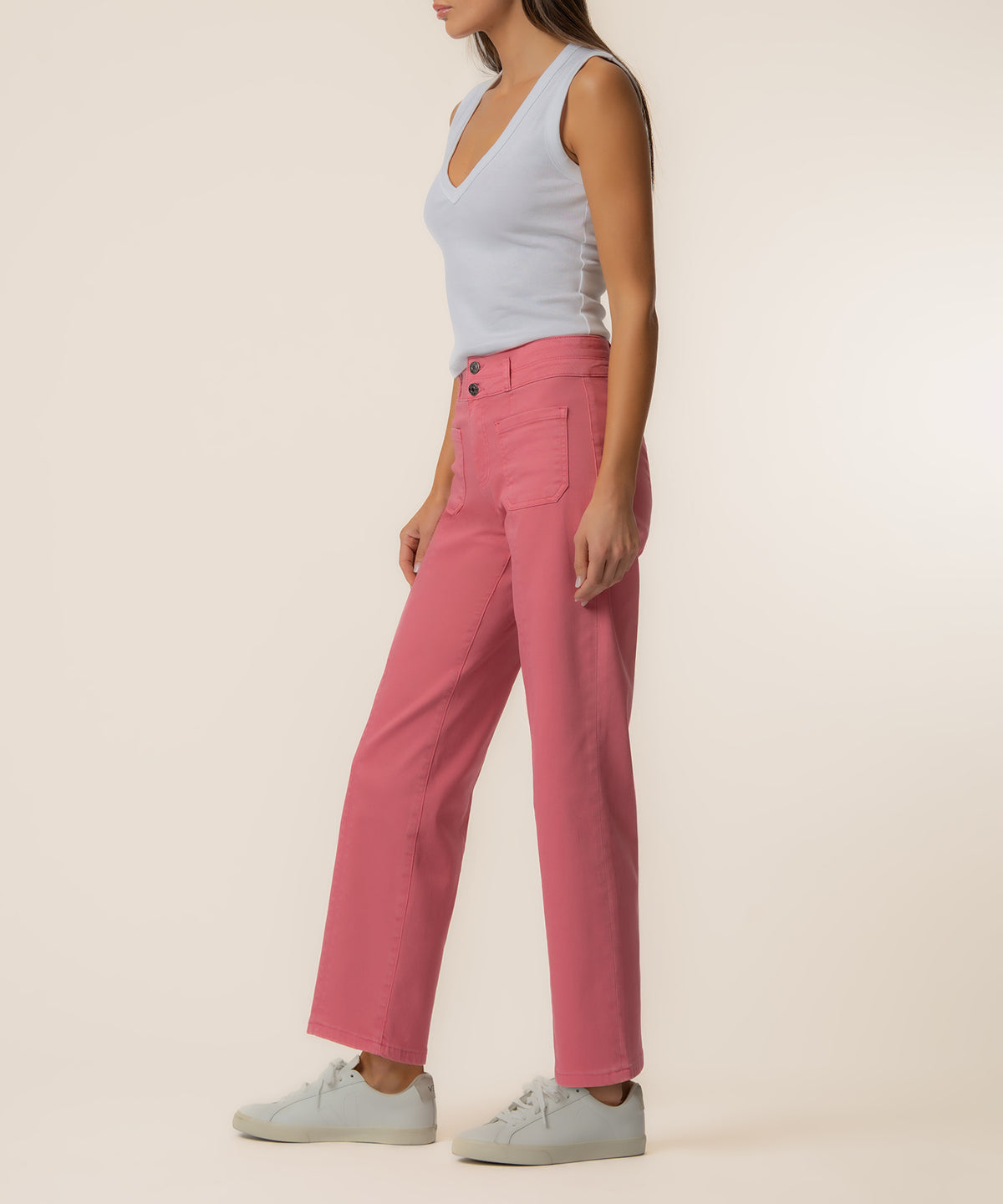 Woman wearing flamingo pink high-rise straight leg jeans with a light blue sleeveless top and white sneakers.