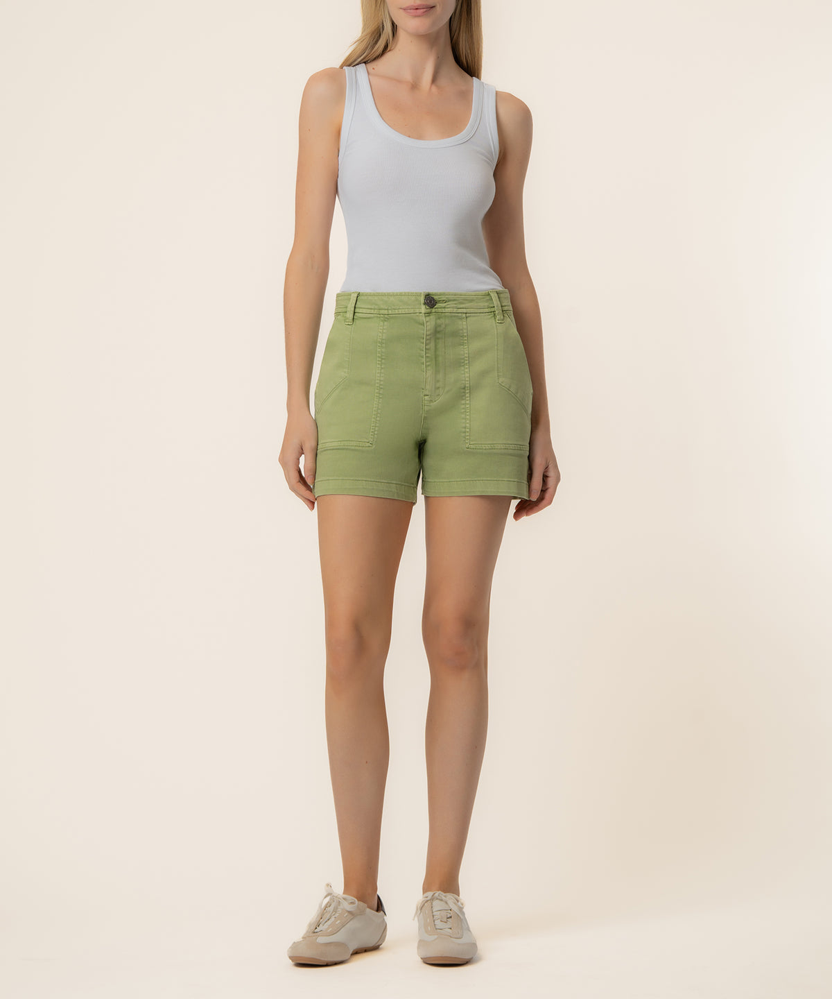 Woman wearing light gray tank top and celery green high-rise shorts with front pockets and button closure.
