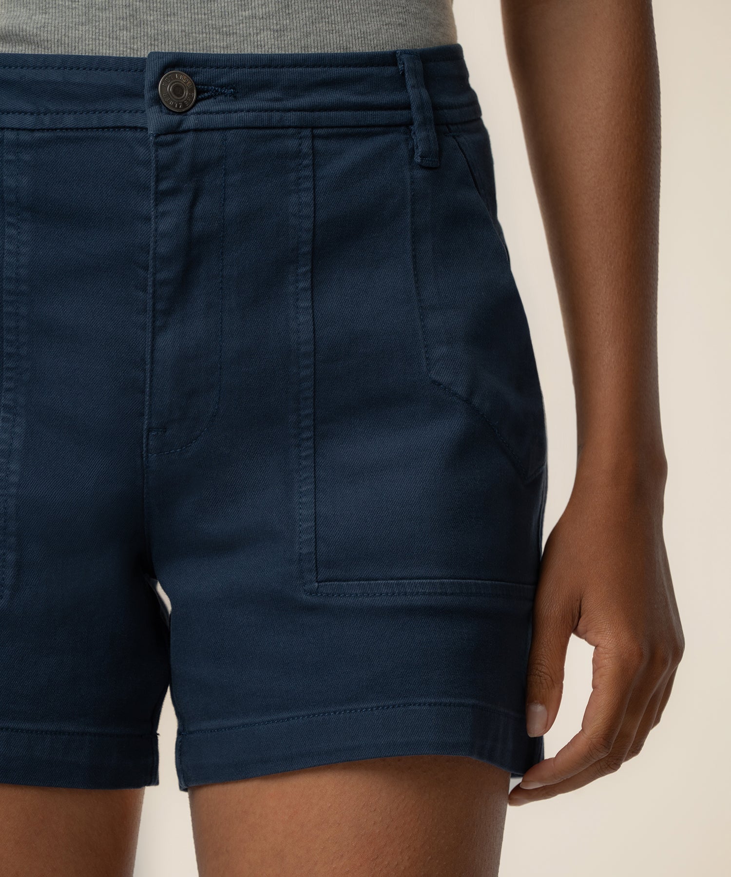 Navy high-rise shorts with button closure and front pockets, shown on model wearing gray top.