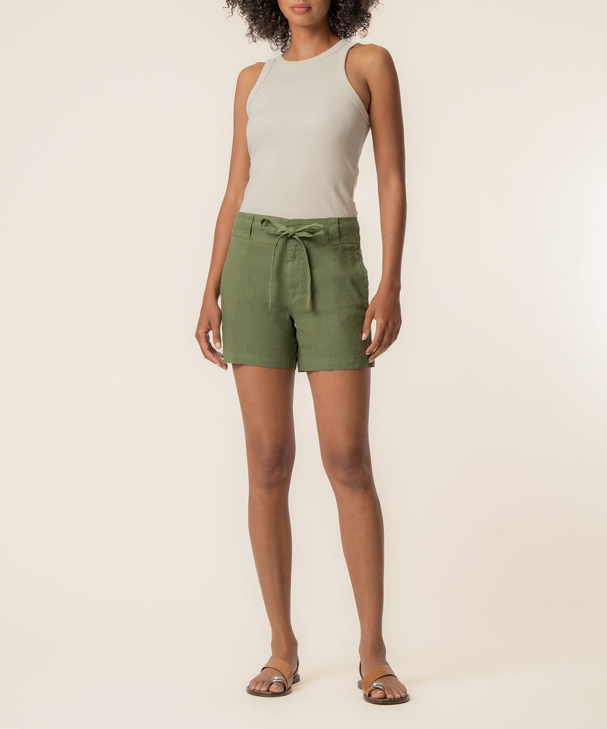 High-rise linen shorts in dill green with tie waist, shown on model with cream tank top.