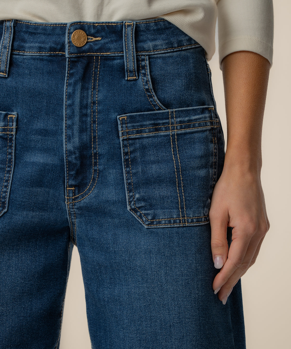 Dark blue high-rise wide-leg jeans with front pockets and tan stitching, worn with a cream ribbed long-sleeve top.