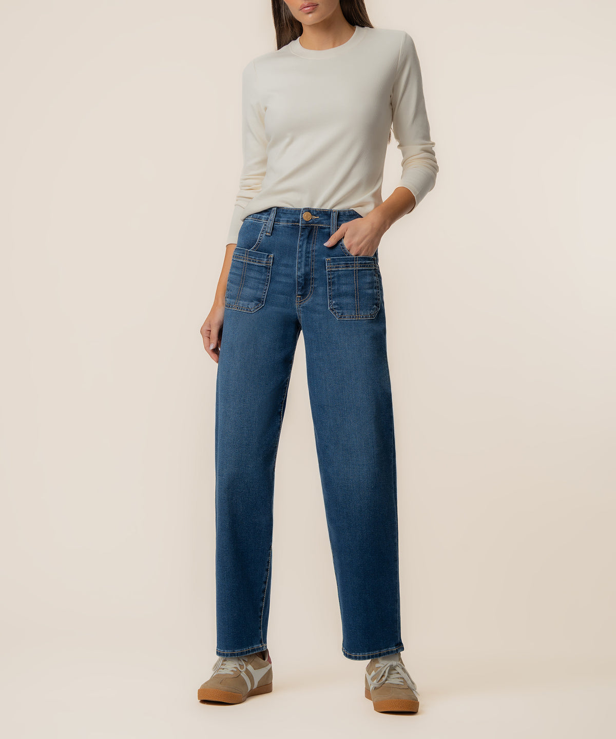 Woman wearing cream long-sleeve shirt tucked into high-rise wide-leg blue jeans with patch pockets.