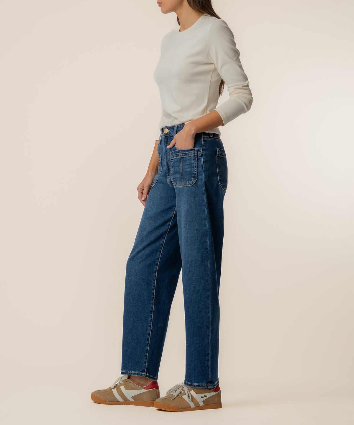 Woman wearing cream long-sleeve top and high-rise dark blue wide-leg jeans with rolled cuffs.