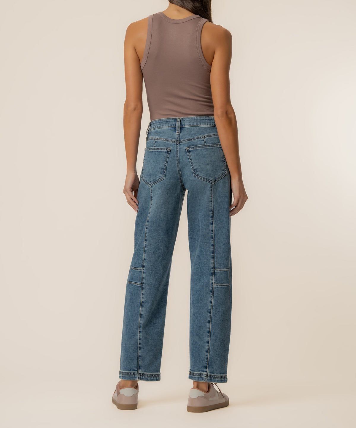 Woman wearing taupe sleeveless tank top and high-rise blue barrel leg jeans with visible seaming detail.
