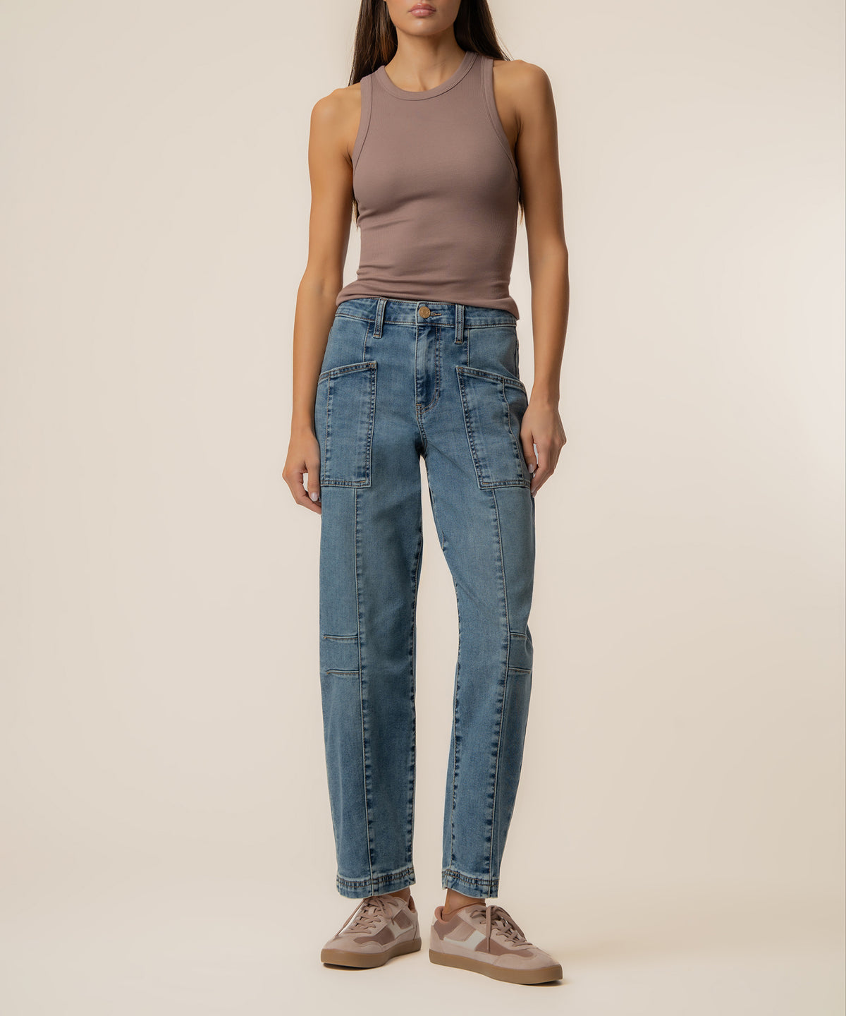 Woman wearing high-rise blue denim barrel leg jeans with cargo pockets and a taupe sleeveless tank top.