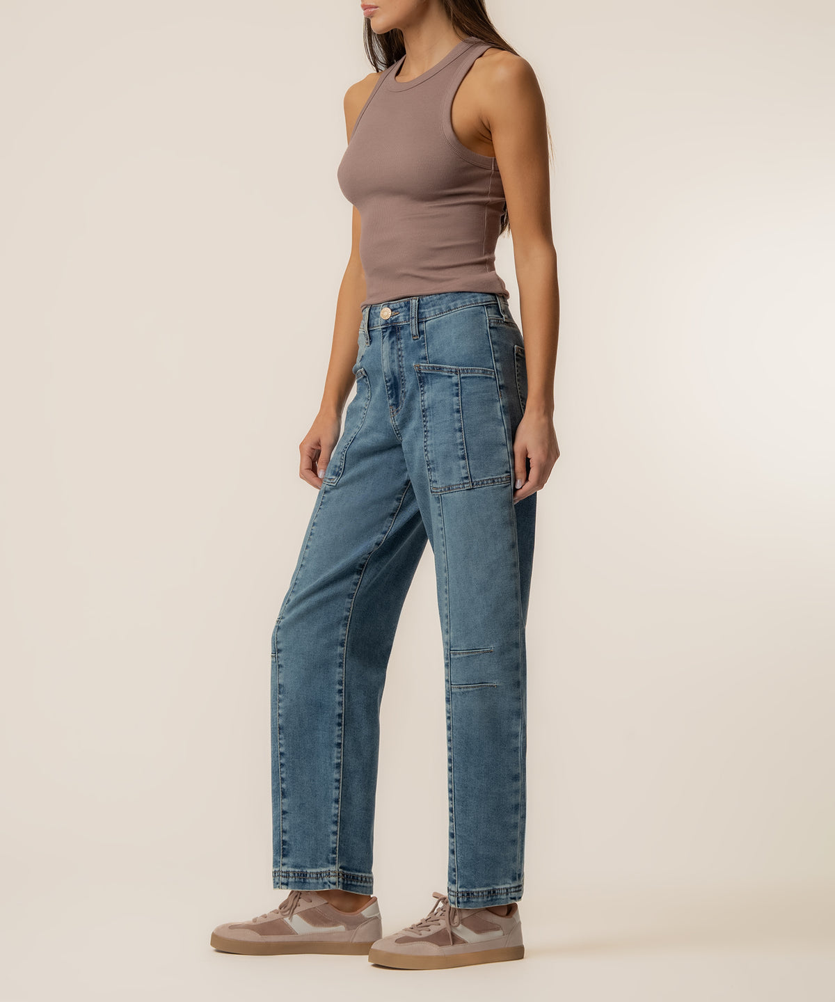 Woman wearing a taupe sleeveless tank top and high-rise blue barrel leg jeans with patch pockets.