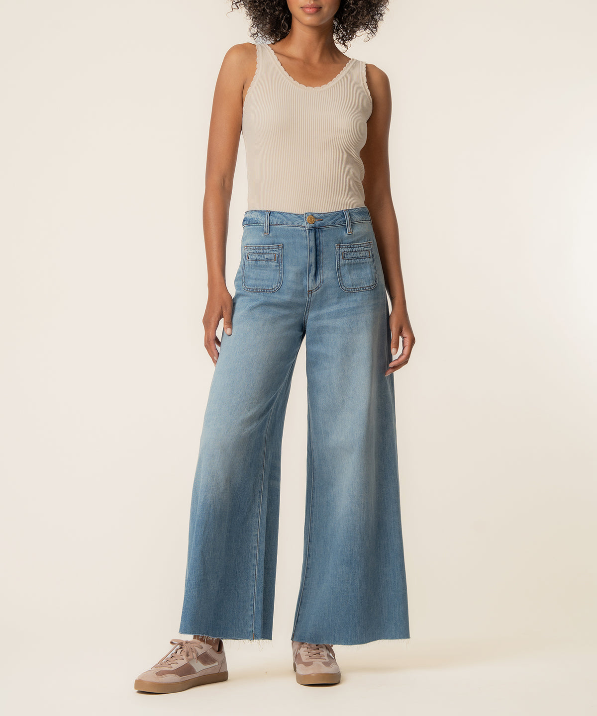 Woman wearing high-rise light blue jeans with wide legs and a cream ribbed tank top.