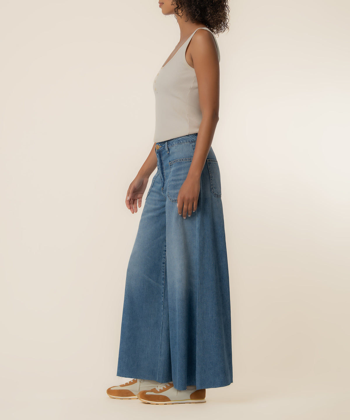 Woman wearing high-rise wide-leg denim jeans in medium blue wash with a white sleeveless top.