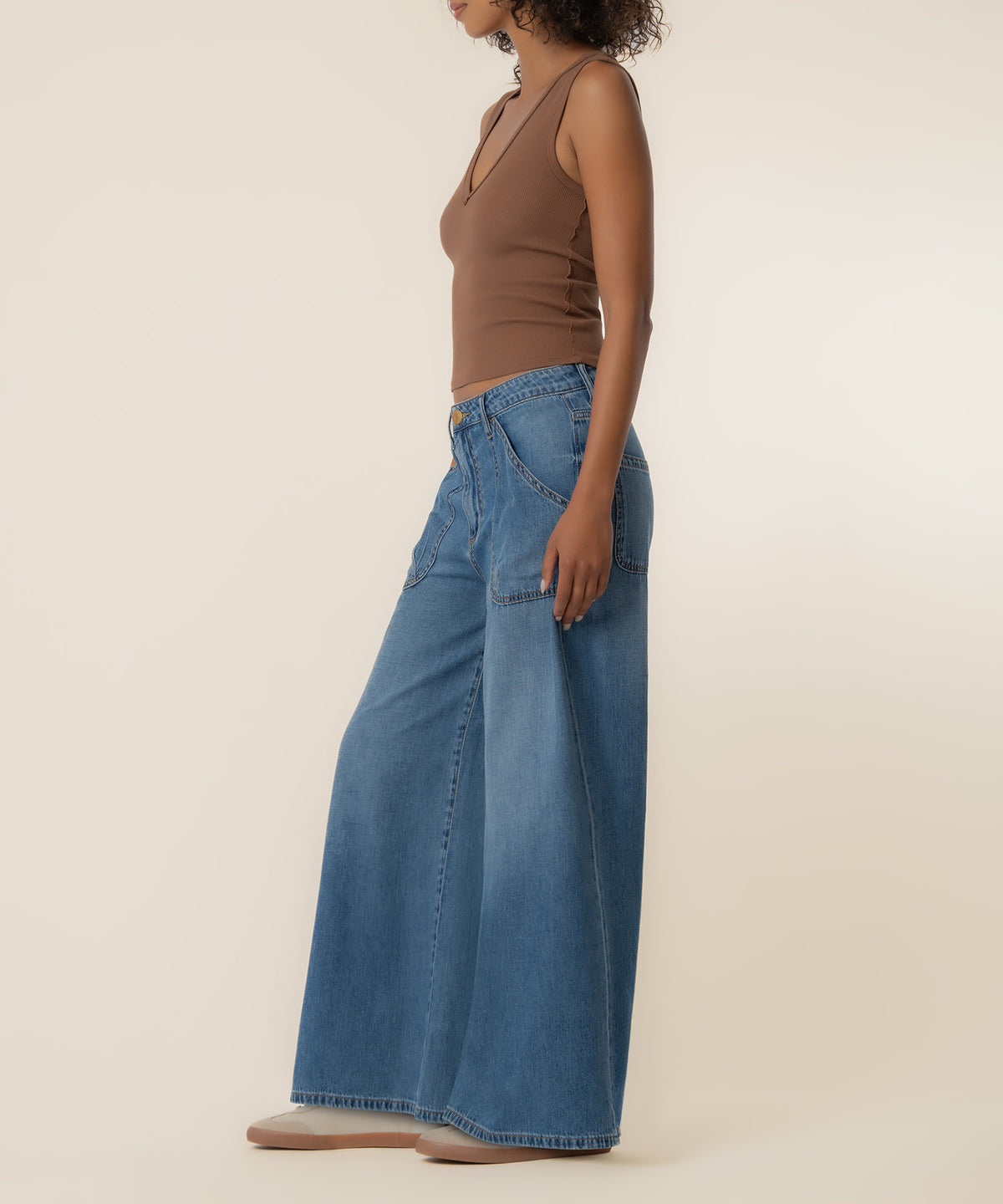 Woman wearing high-rise super wide-leg denim jeans in medium blue wash with brown sleeveless top, side view.