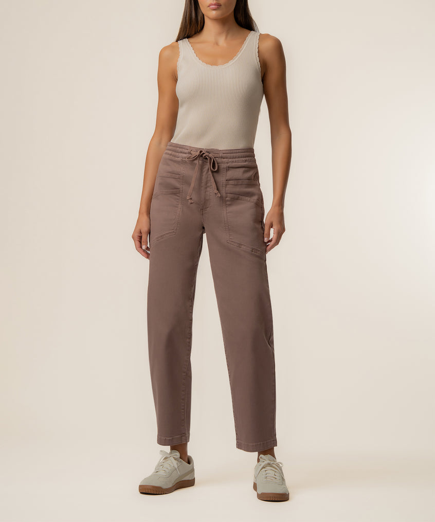 Woman wearing mocha high-rise relaxed leg jeans with drawstring waist and a cream ribbed tank top.