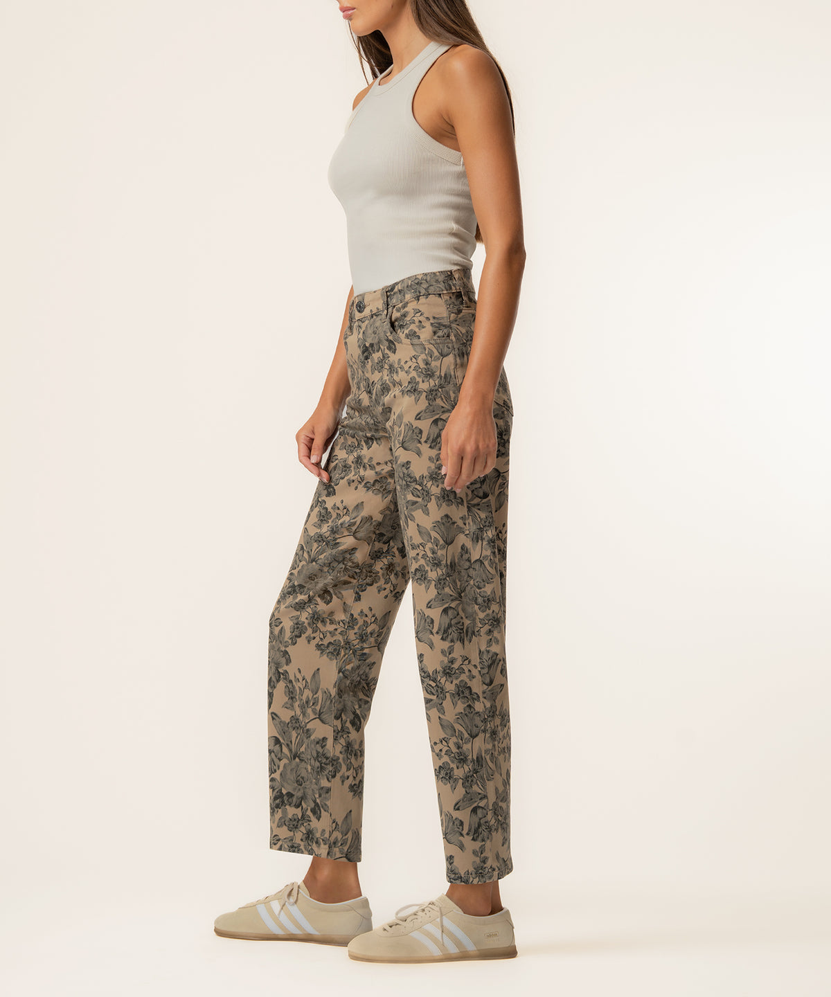 Woman wearing sand-colored high-rise relaxed-leg pants with dark floral print and a white sleeveless tank top.