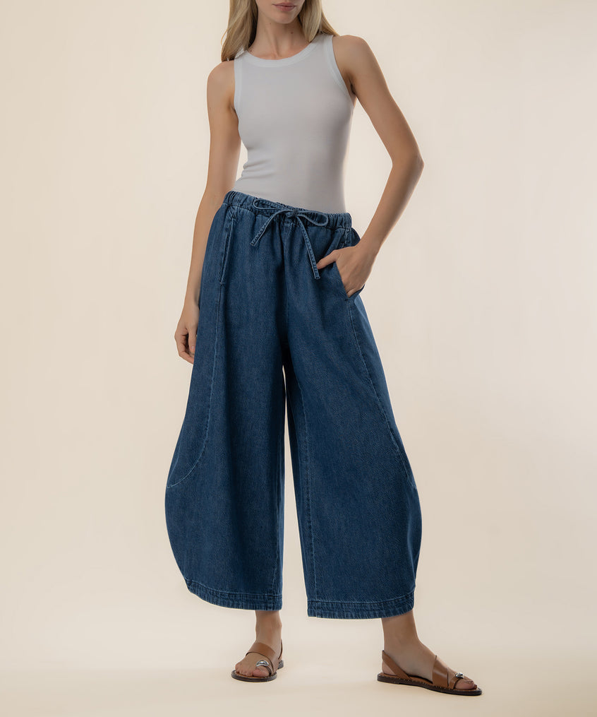 Woman wearing light gray sleeveless tank top and dark blue denim barrel-leg jeans with drawstring waist and side pockets.