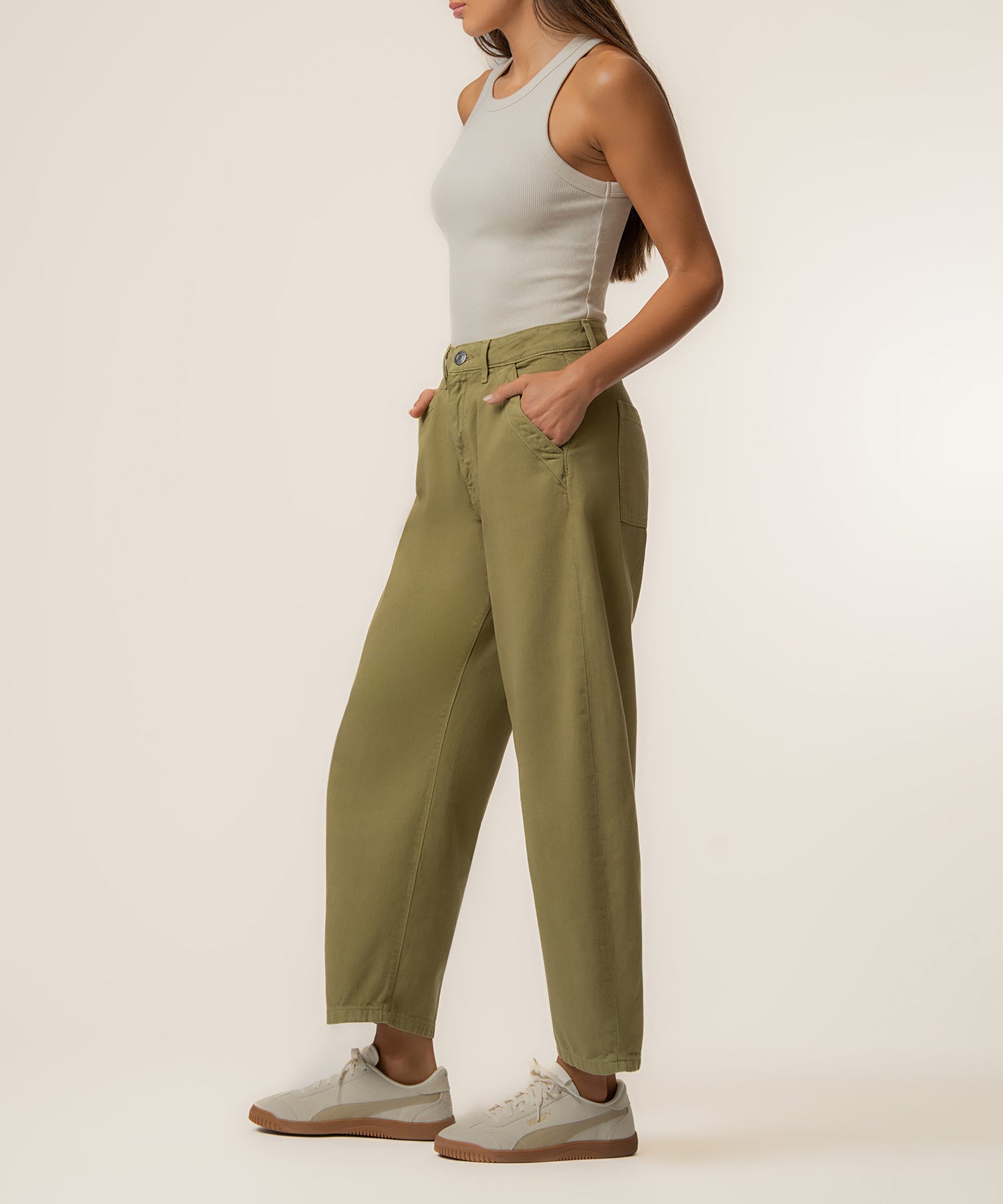 Woman wearing high-rise relaxed-leg trousers in olive green with a white tank top and cream sneakers.