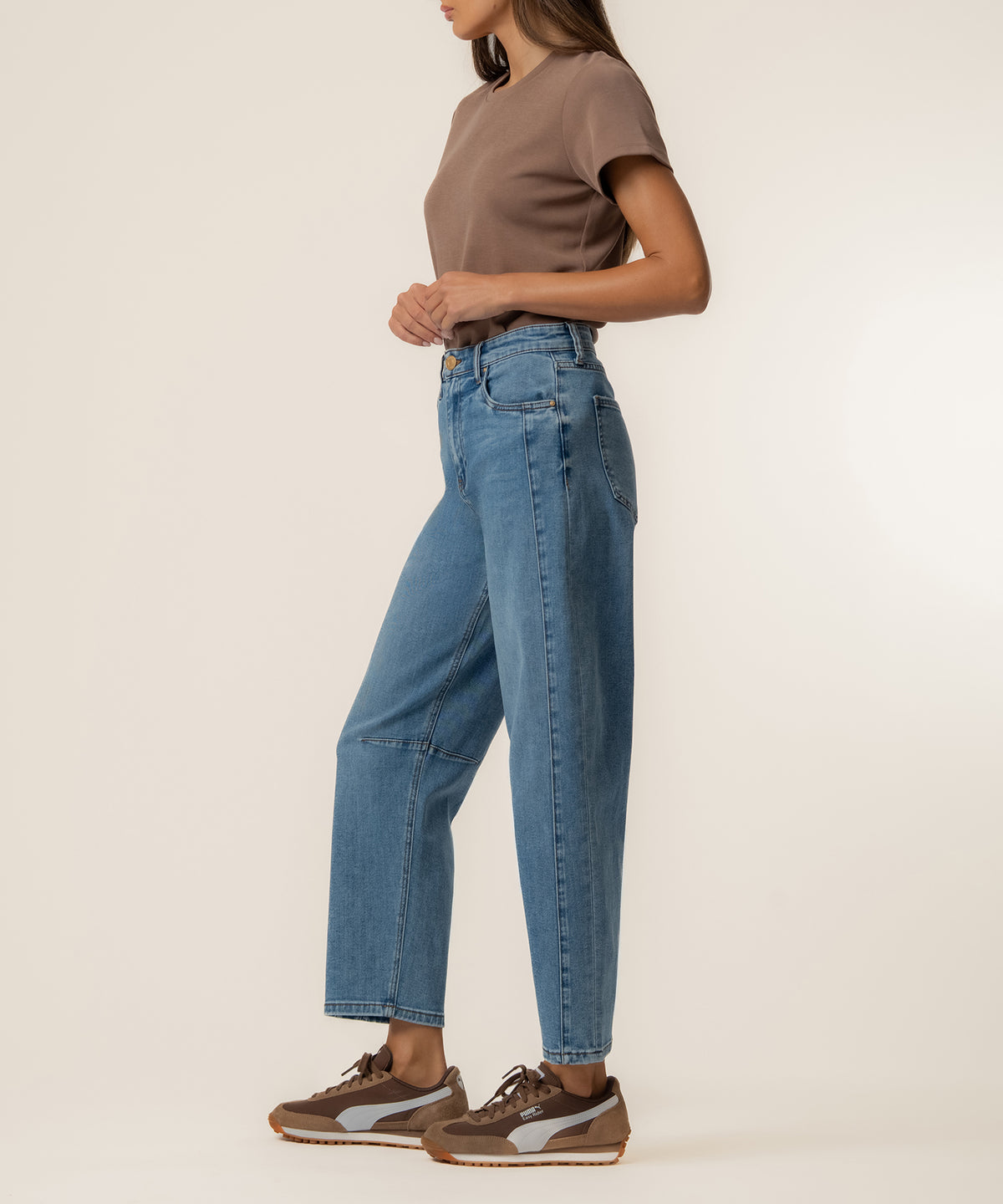 Woman wearing blue high-rise relaxed-fit jeans with a taupe t-shirt and brown sneakers.