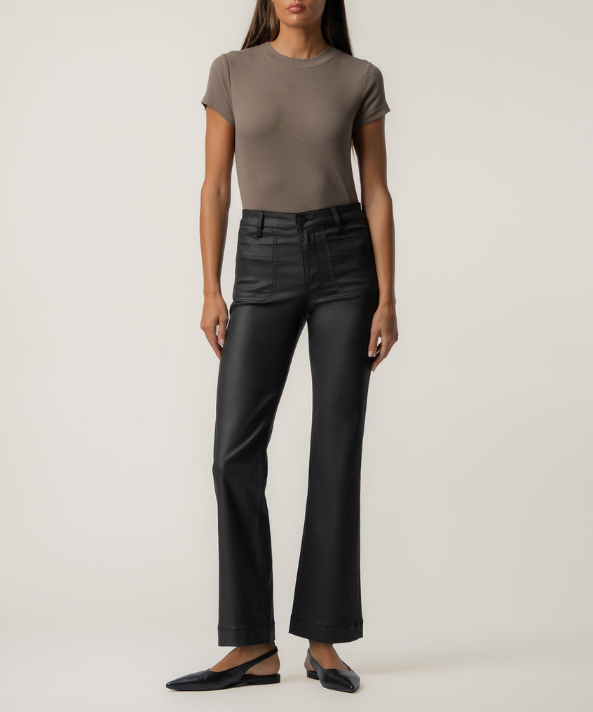 A woman wears high-rise black coated flare pants with front patch pockets, a taupe fitted short-sleeve top, and black pointed slingback flats.
