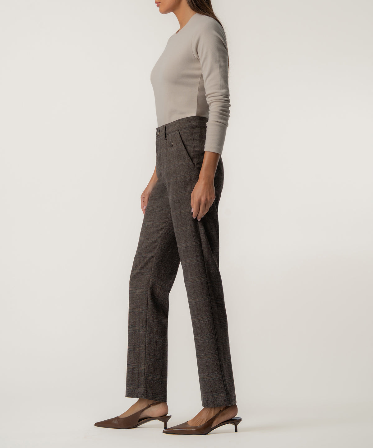 A woman in profile wears high-rise dark brown plaid trousers with a fitted beige long-sleeve top and brown slingback kitten heels.