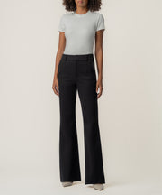 A woman stands facing forward in high-rise black flare pants, a fitted light gray short-sleeve top, and pointed beige shoes.