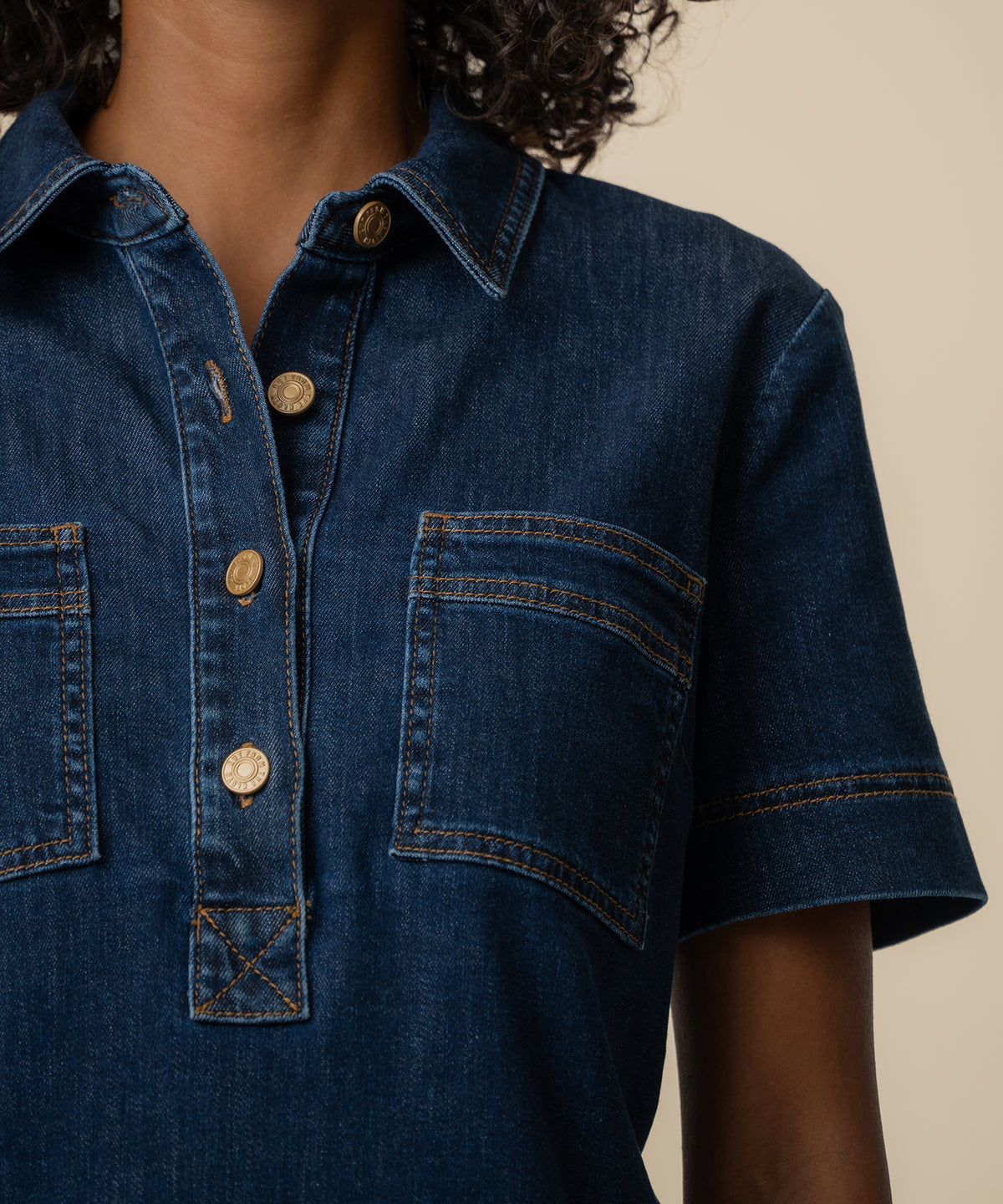 Dark blue denim dress with collar, short sleeves, gold buttons, and chest pockets with contrasting stitching.