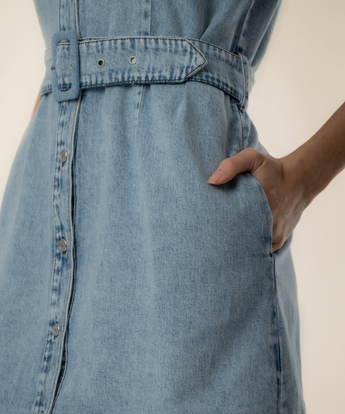 Light blue denim halter dress with front button closure, belted waist, and side pocket.
