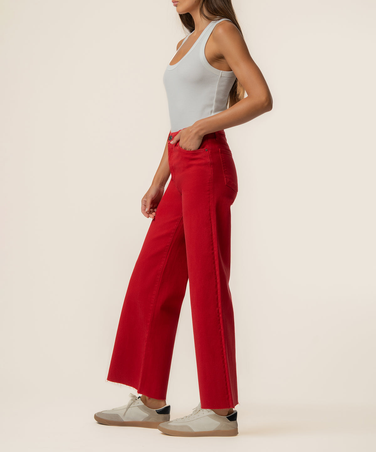 Woman wearing ruby red high-rise wide leg jeans with white tank top and cream sneakers.