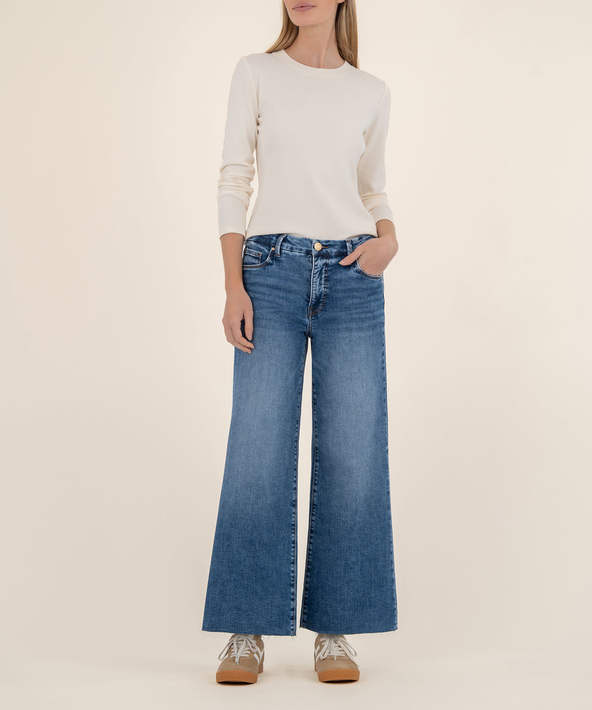 Woman wearing cream long-sleeve top and blue high-rise wide-leg jeans with tan platform shoes.