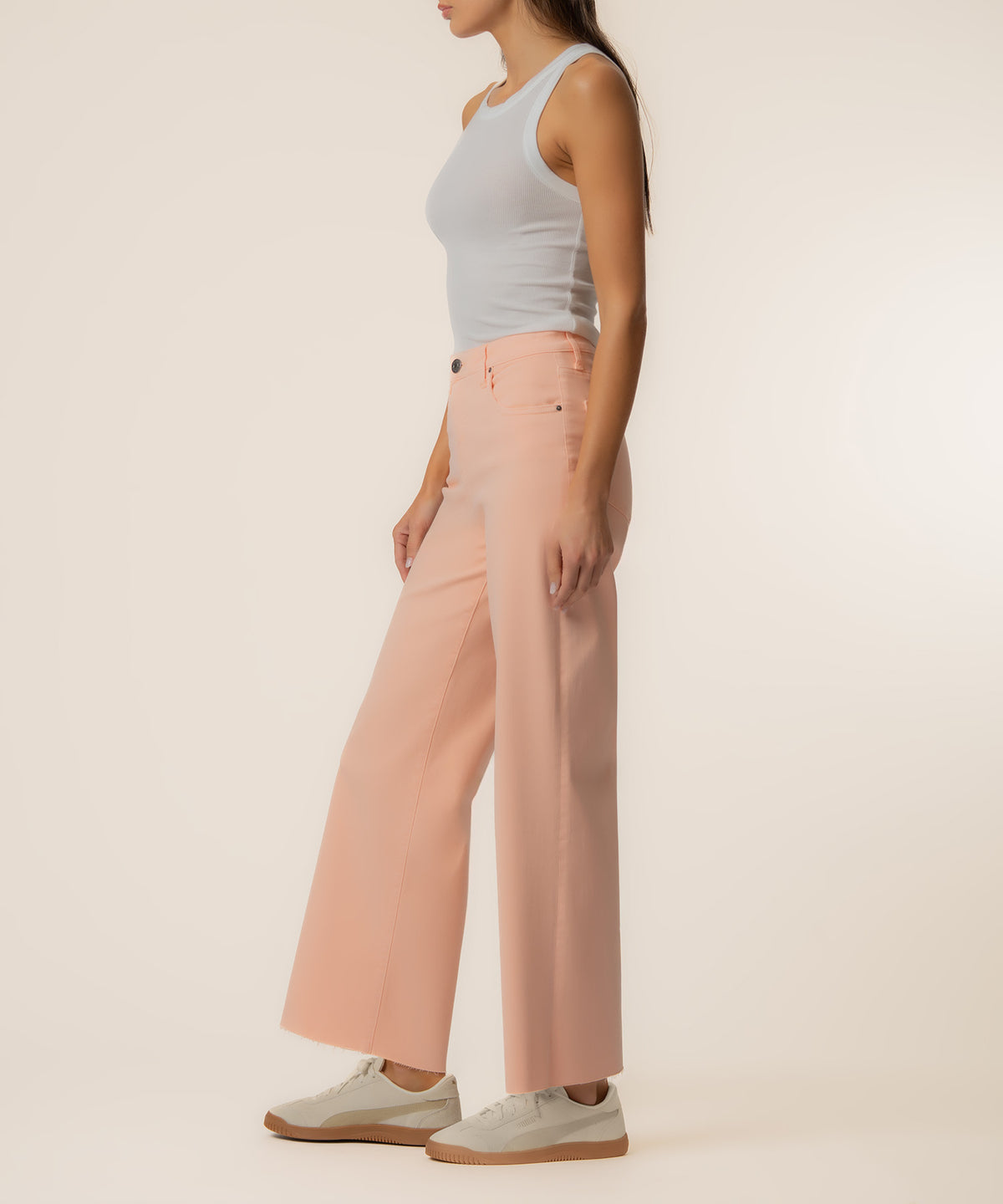 Woman wearing light blue sleeveless tank top and peach-colored high-rise wide-leg pants with white sneakers.