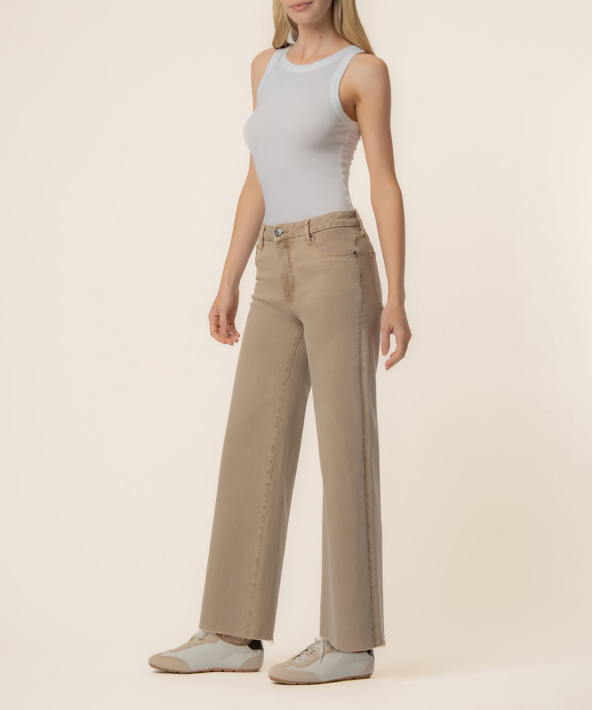 Woman wearing a beige high-rise wide-leg jean with a white sleeveless tank top and white sneakers.