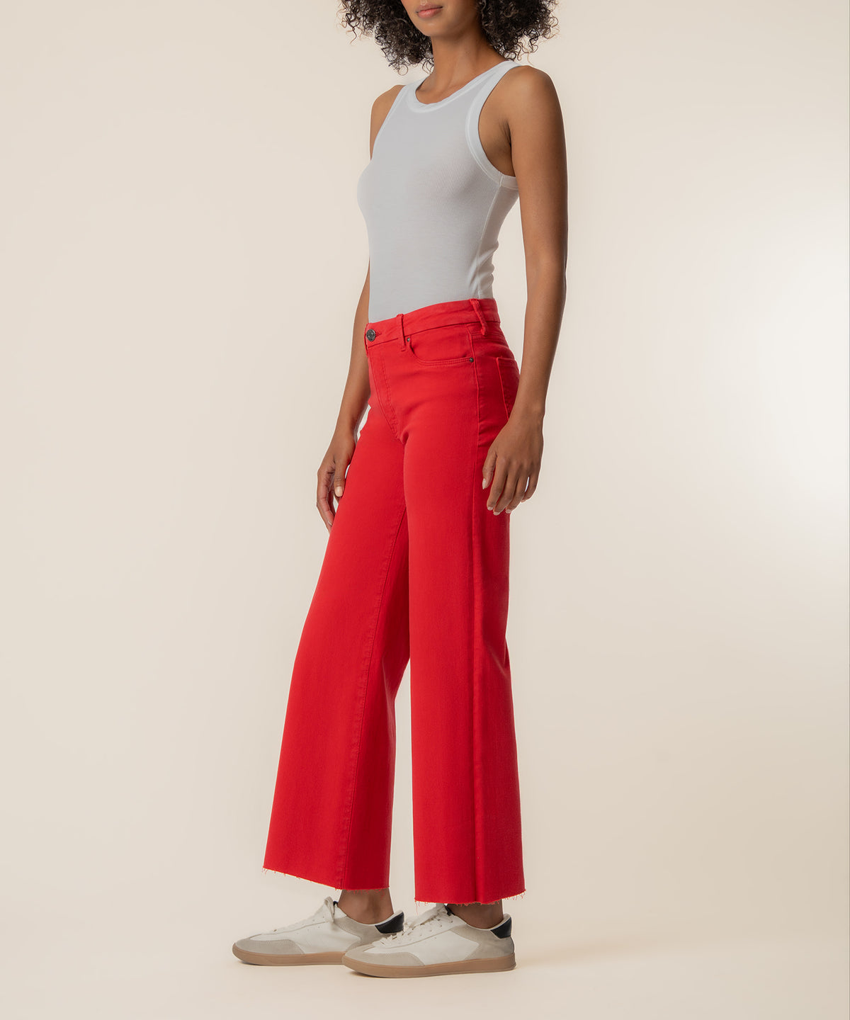 Woman wearing white sleeveless tank top and red high-rise wide-leg jeans with white sneakers.