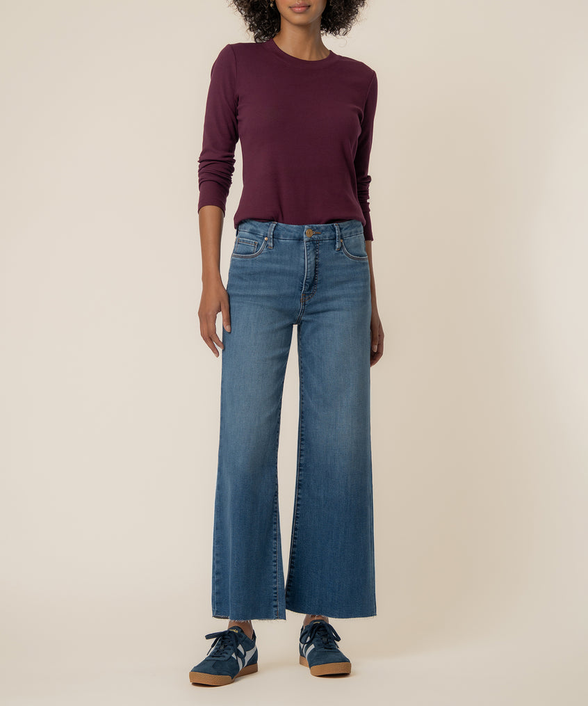 Woman wearing high-rise wide-leg jeans in medium blue denim with a burgundy long-sleeve top.