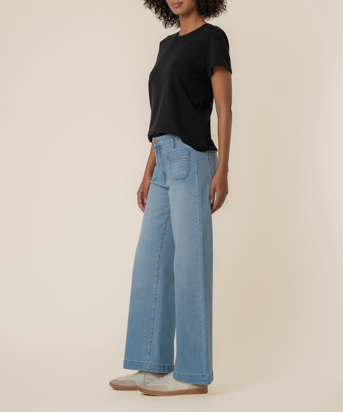 Woman wearing light blue high-rise wide-leg jeans with a black t-shirt and cream sneakers.