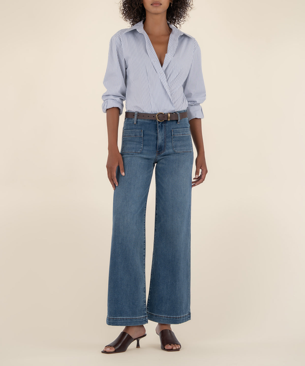 Woman wearing blue striped wrap blouse with high-rise wide-leg jeans in medium wash and brown belt.