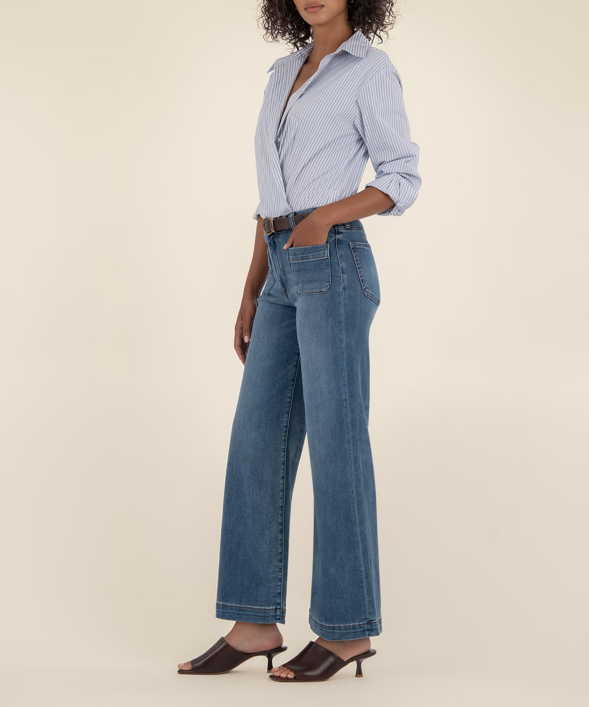 Woman wearing light blue striped button-up shirt and medium wash wide-leg jeans with high rise waistband.
