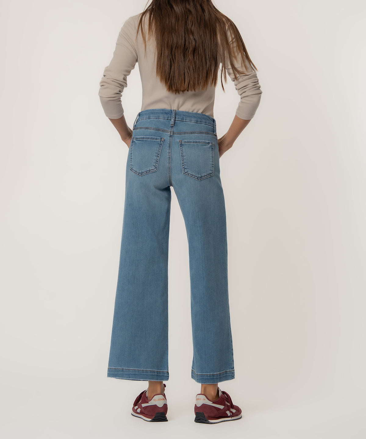 Woman wearing light blue high-rise wide-leg jeans with cropped hem, shown from back view with cream long-sleeve top.