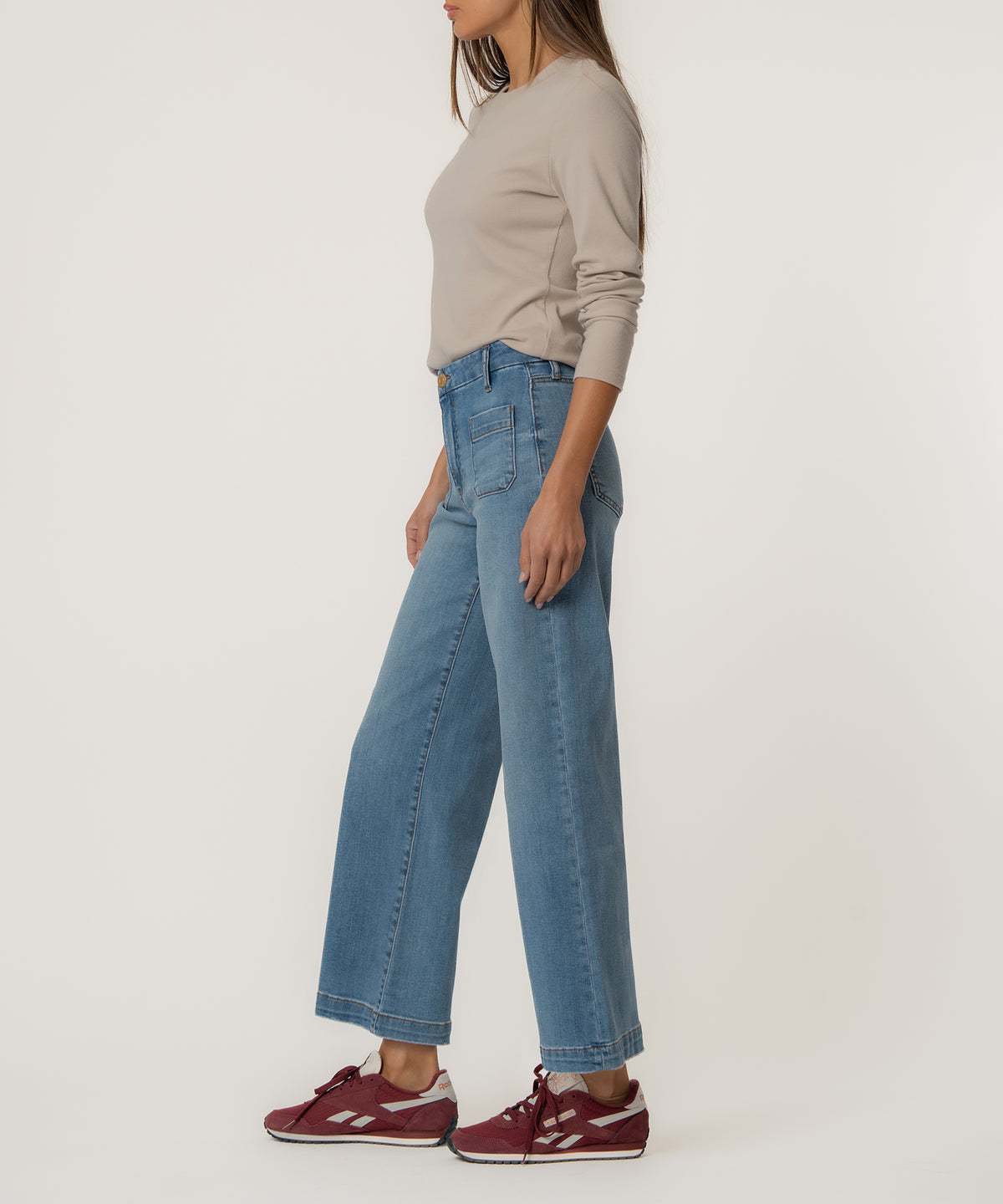 Woman wearing light blue high-rise wide-leg jeans with a beige long-sleeve top and burgundy sneakers.