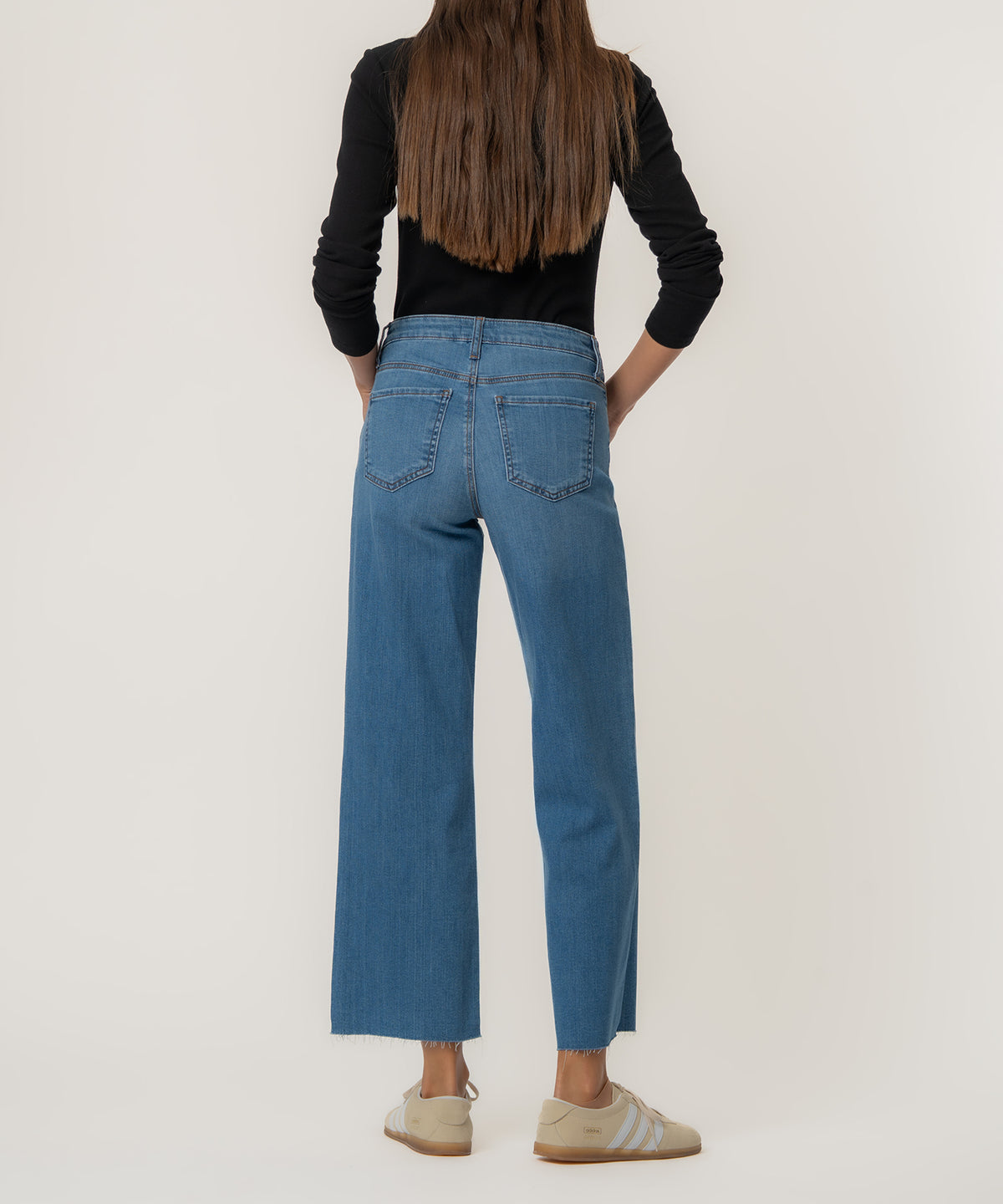 Woman wearing high-rise wide-leg jeans in medium blue denim with cropped raw hem, styled with black long-sleeve top.
