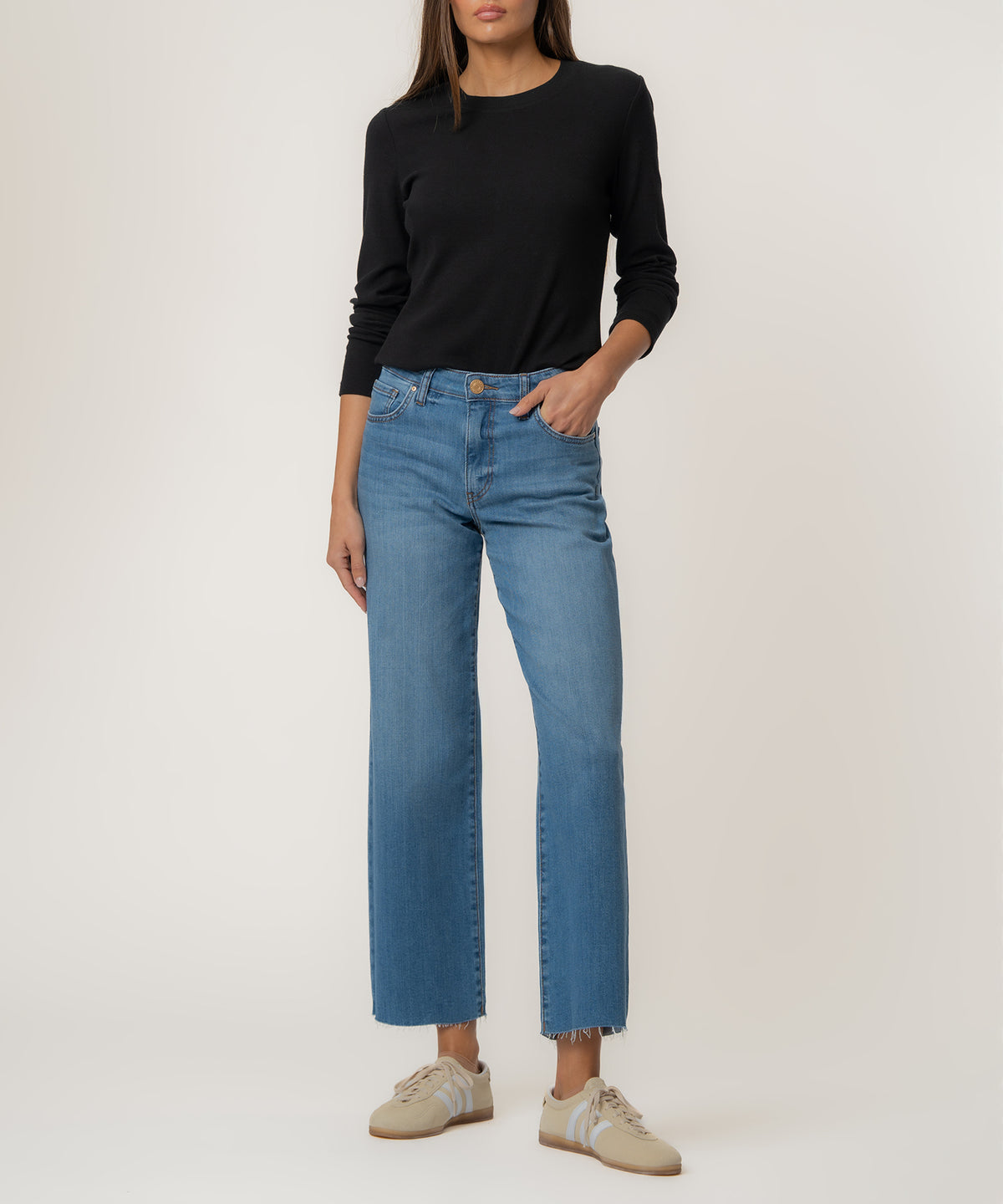 Woman wearing black long-sleeve top and medium-wash wide-leg cropped jeans with frayed hem and cream sneakers.