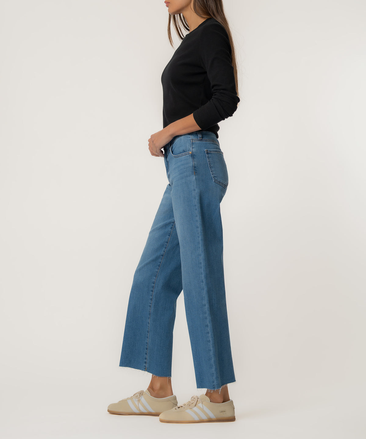 Woman wearing high-rise wide-leg jeans in medium blue wash with black long-sleeve top and cream sneakers.