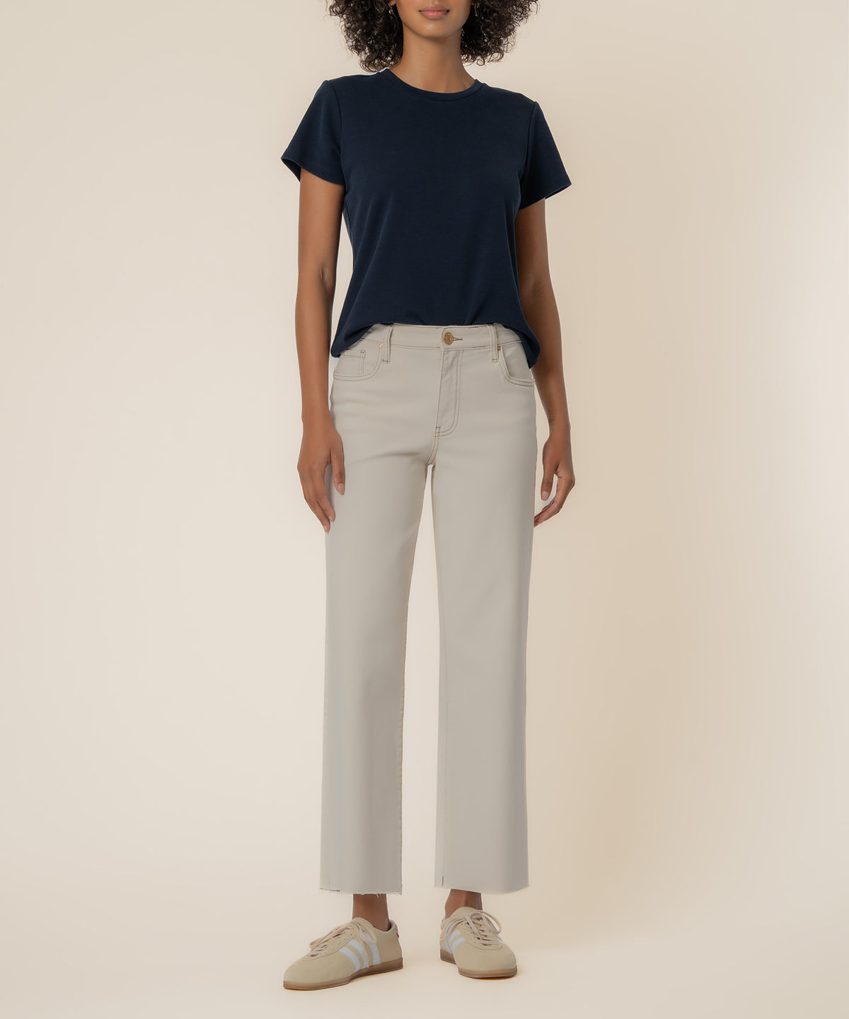 Woman wearing ecru high-rise wide-leg pants with navy short-sleeve t-shirt and beige sneakers.