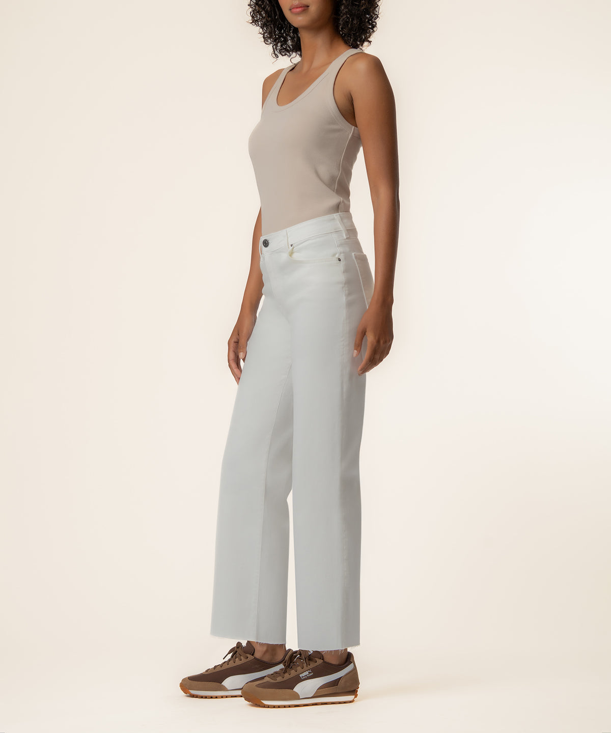 Woman wearing high-rise white wide-leg jeans with a beige tank top and brown and white sneakers.