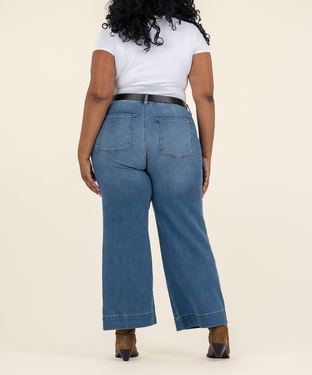 Back view of a person wearing medium-wash high-rise wide-leg jeans with a black belt, white top, and brown ankle boots.