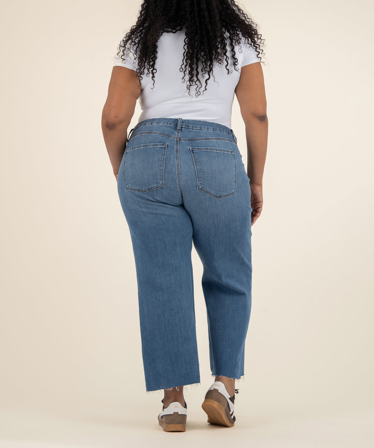 Woman wearing high-rise wide-leg blue jeans with frayed ankles and white t-shirt, back view.
