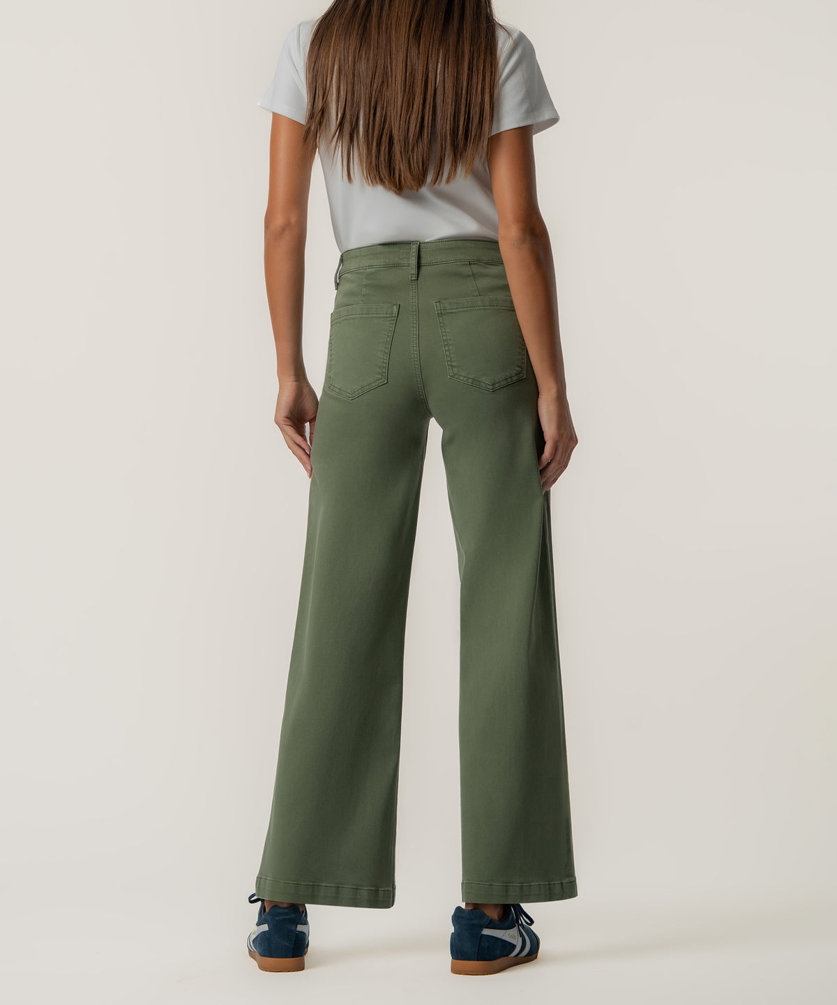 Back view of a person wearing olive green high-rise wide-leg pants with two back pockets, a white t-shirt, and navy sneakers.