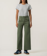 A person stands facing forward in olive green high-rise wide-leg pants with zippered front pockets, a light gray t-shirt, and navy sneakers.