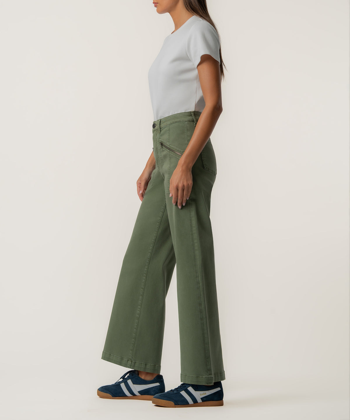 A woman in profile wears high-rise olive green wide-leg pants with a white tee and navy sneakers.