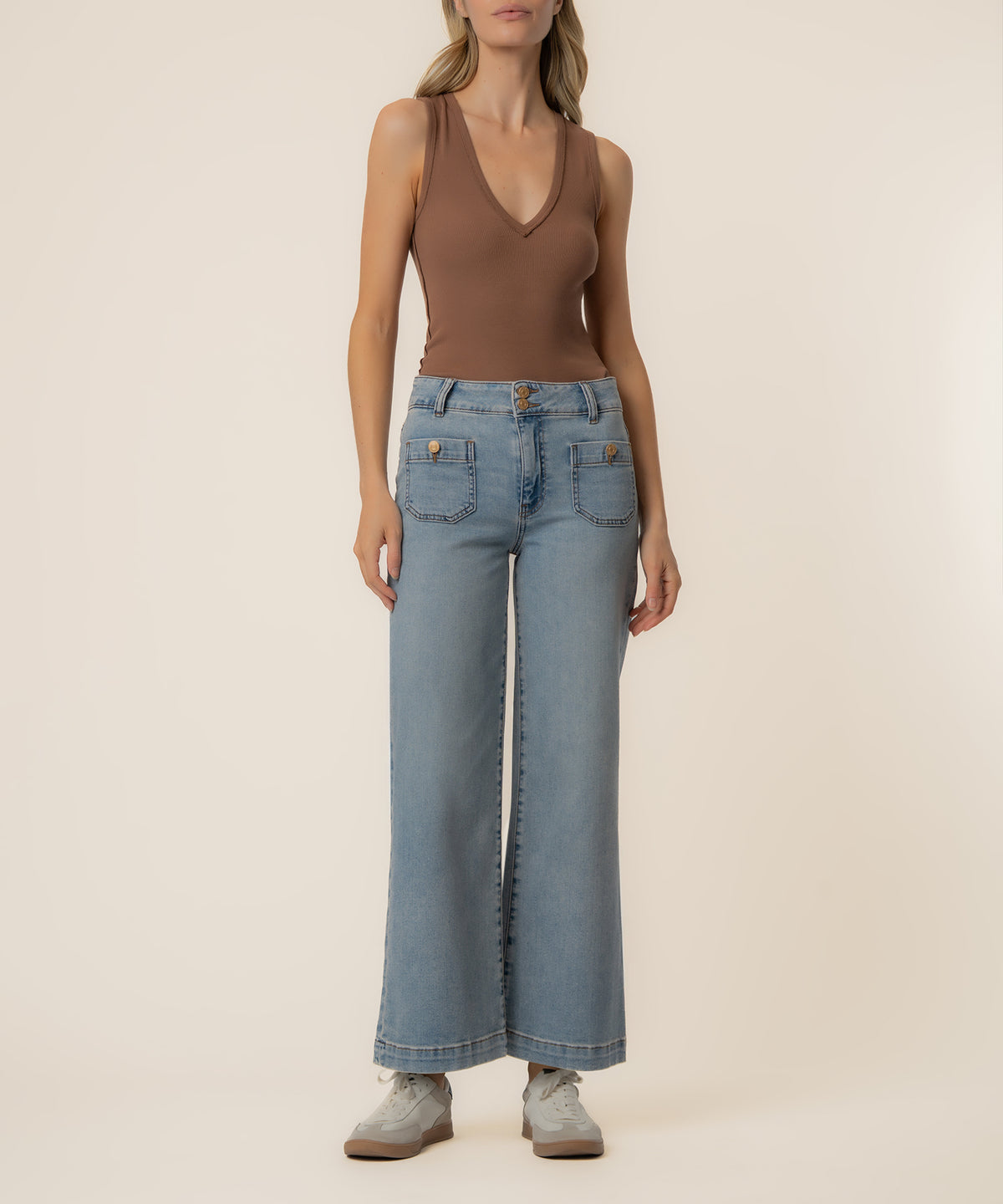 Woman wearing a brown sleeveless V-neck tank top and light blue high-rise wide-leg jeans with gold button details.
