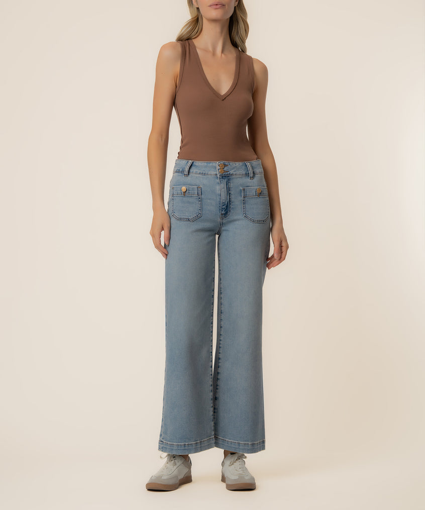 Woman wearing a brown sleeveless V-neck tank top and light blue high-rise wide-leg jeans with gold button details.